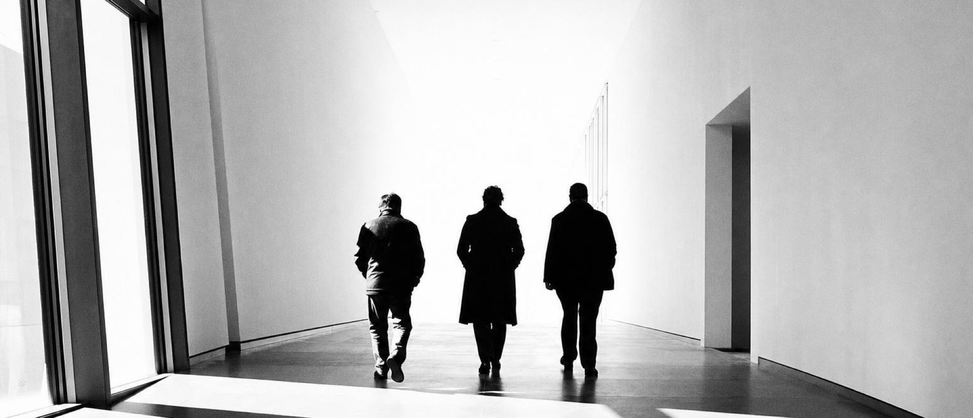 Three people walking out through a bright doorway