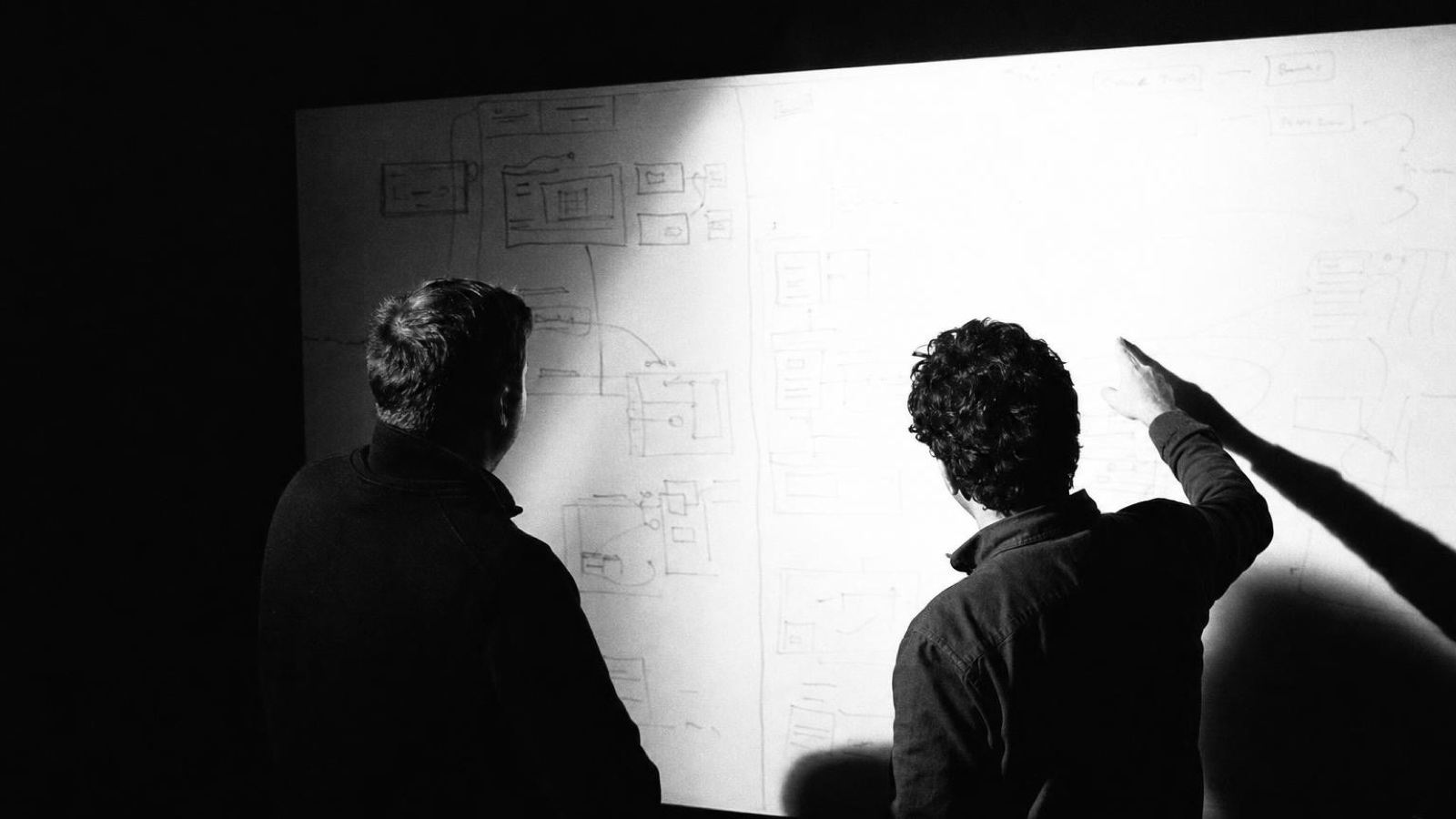 Two people marking up a diagram on a whiteboard, one pointing