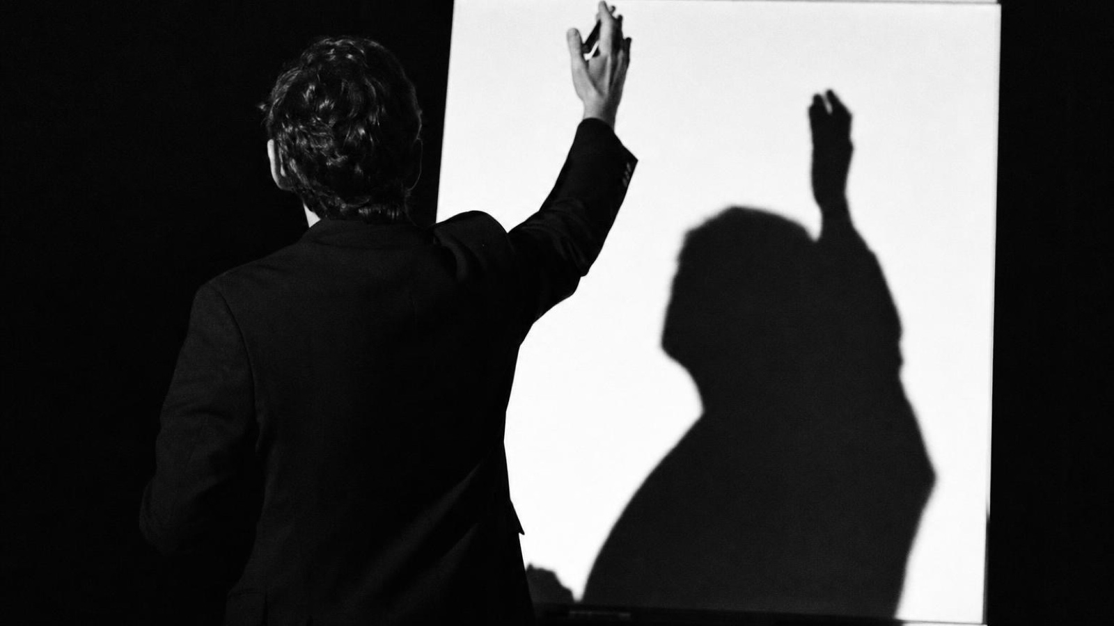 Someone writing on a lit whiteboard, their shadow thrown across it