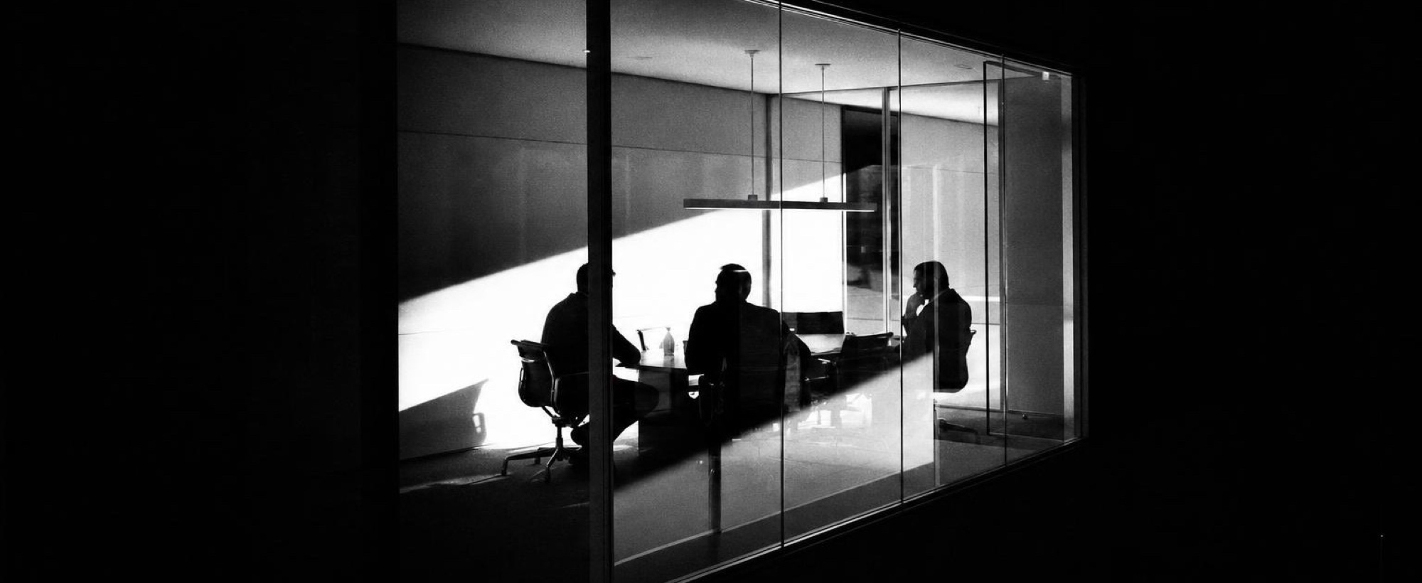 Three people talking in a glass-walled meeting room at night