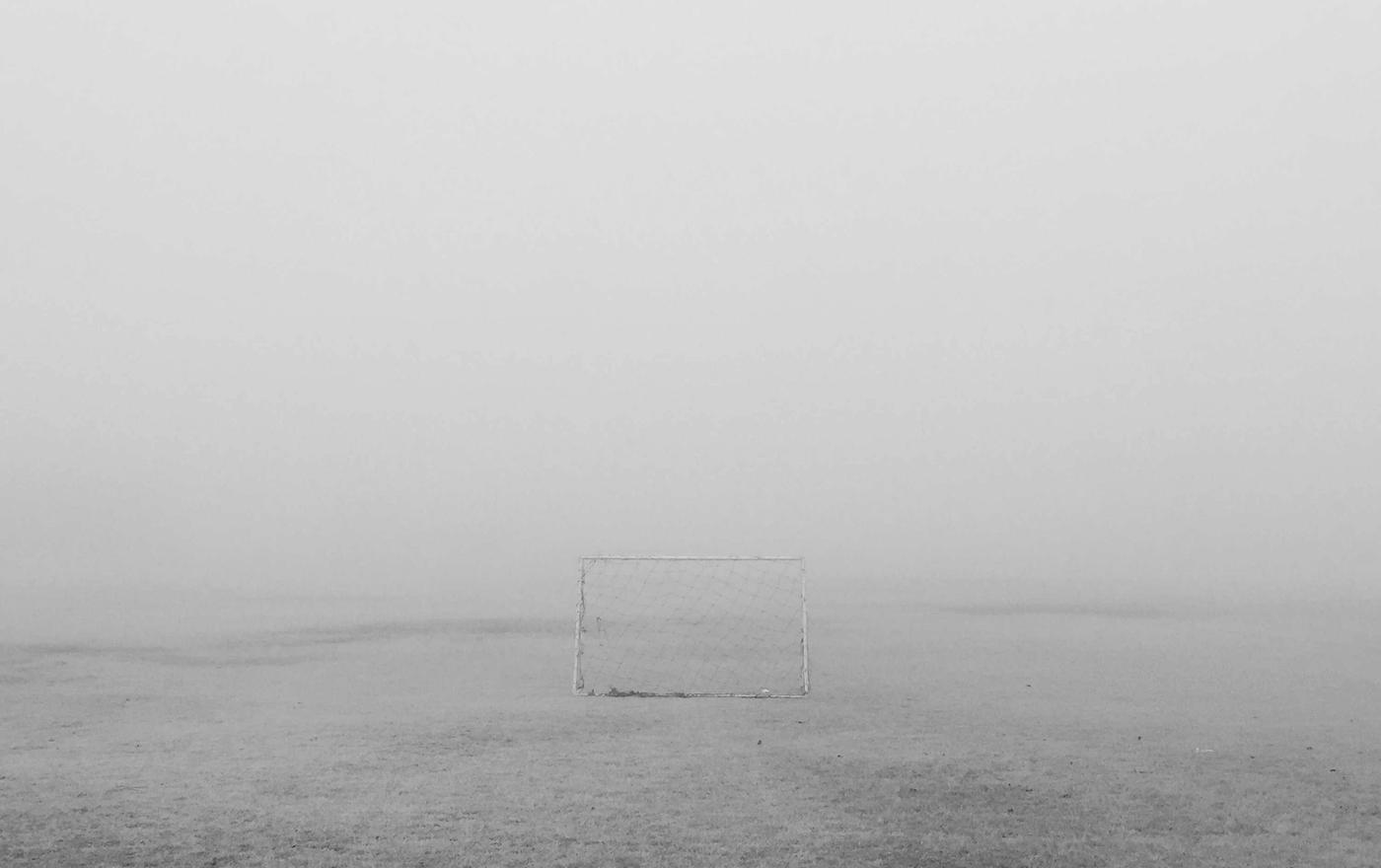A goal frame standing in an empty field in fog