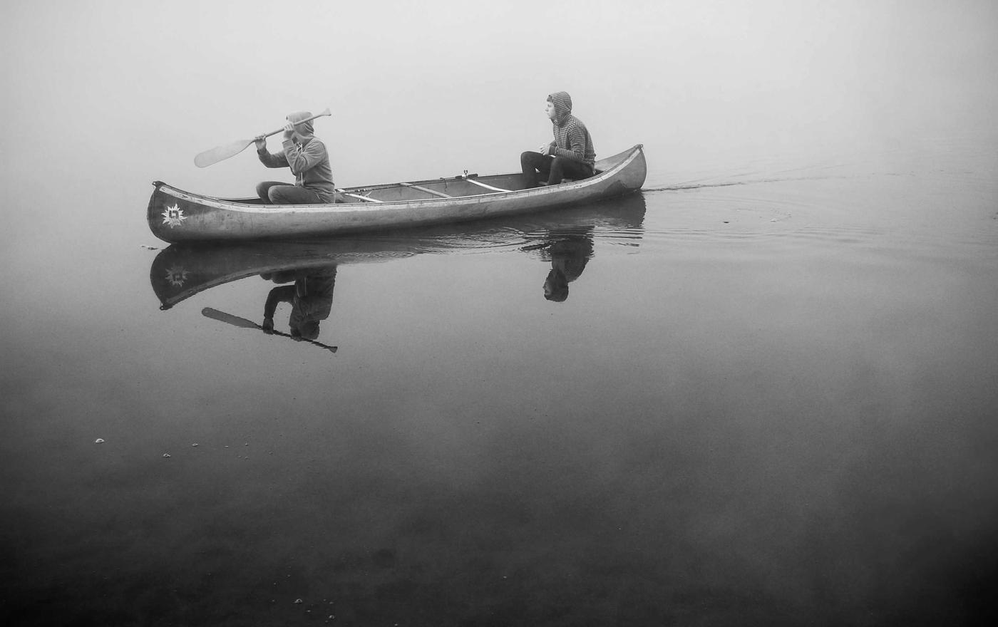 Two people paddling a canoe through mist