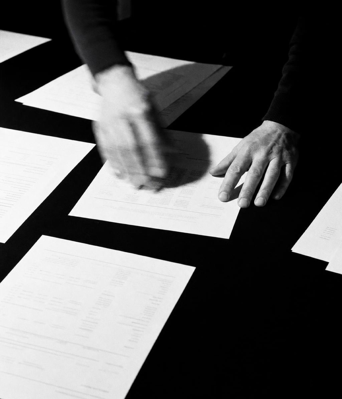 Hands spreading printed statements across a desk