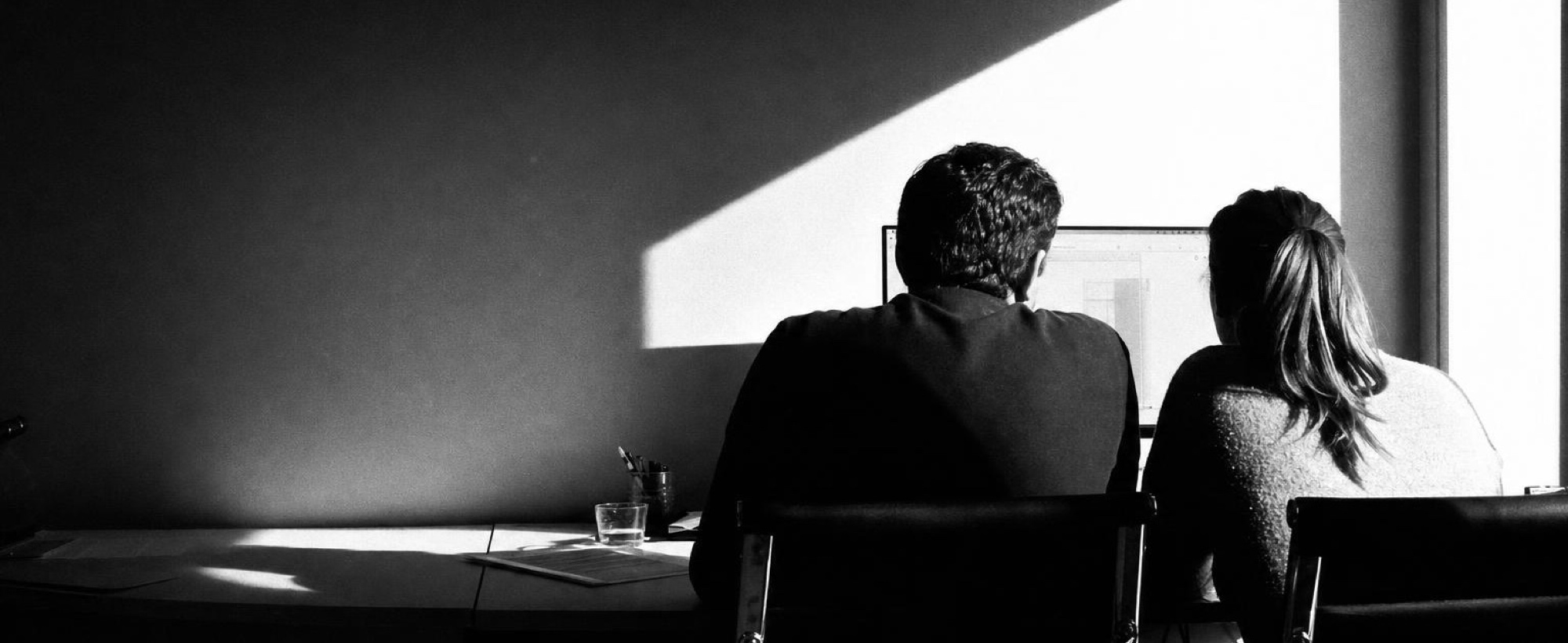 Two people working side by side at a desk, seen from behind