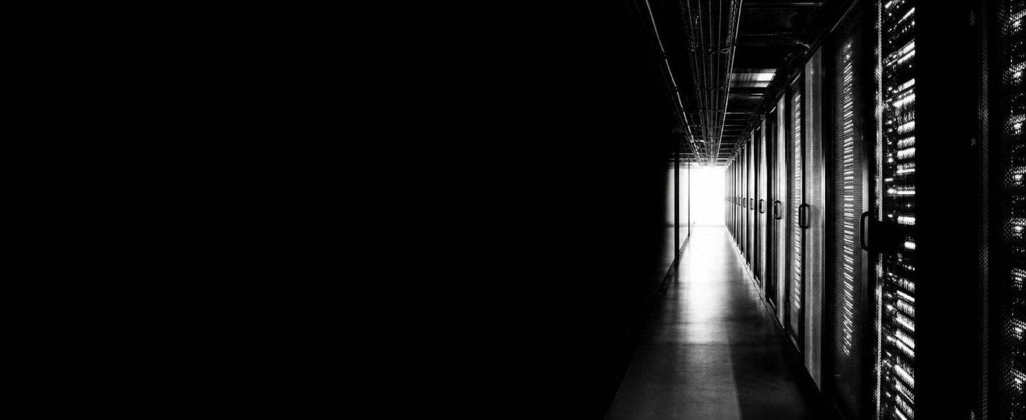 An aisle of server racks running towards a lit doorway