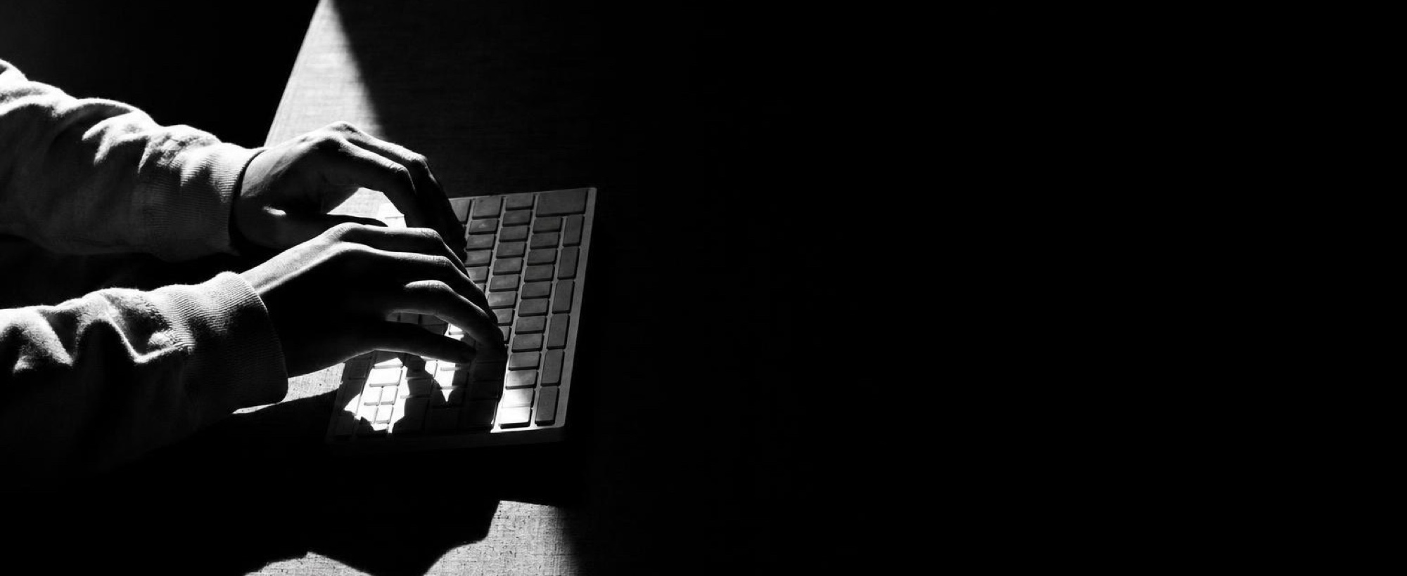 Hands on a laptop keyboard in a darkened room