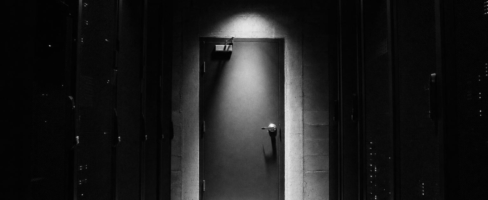 A closed door at the end of a dim server-room corridor