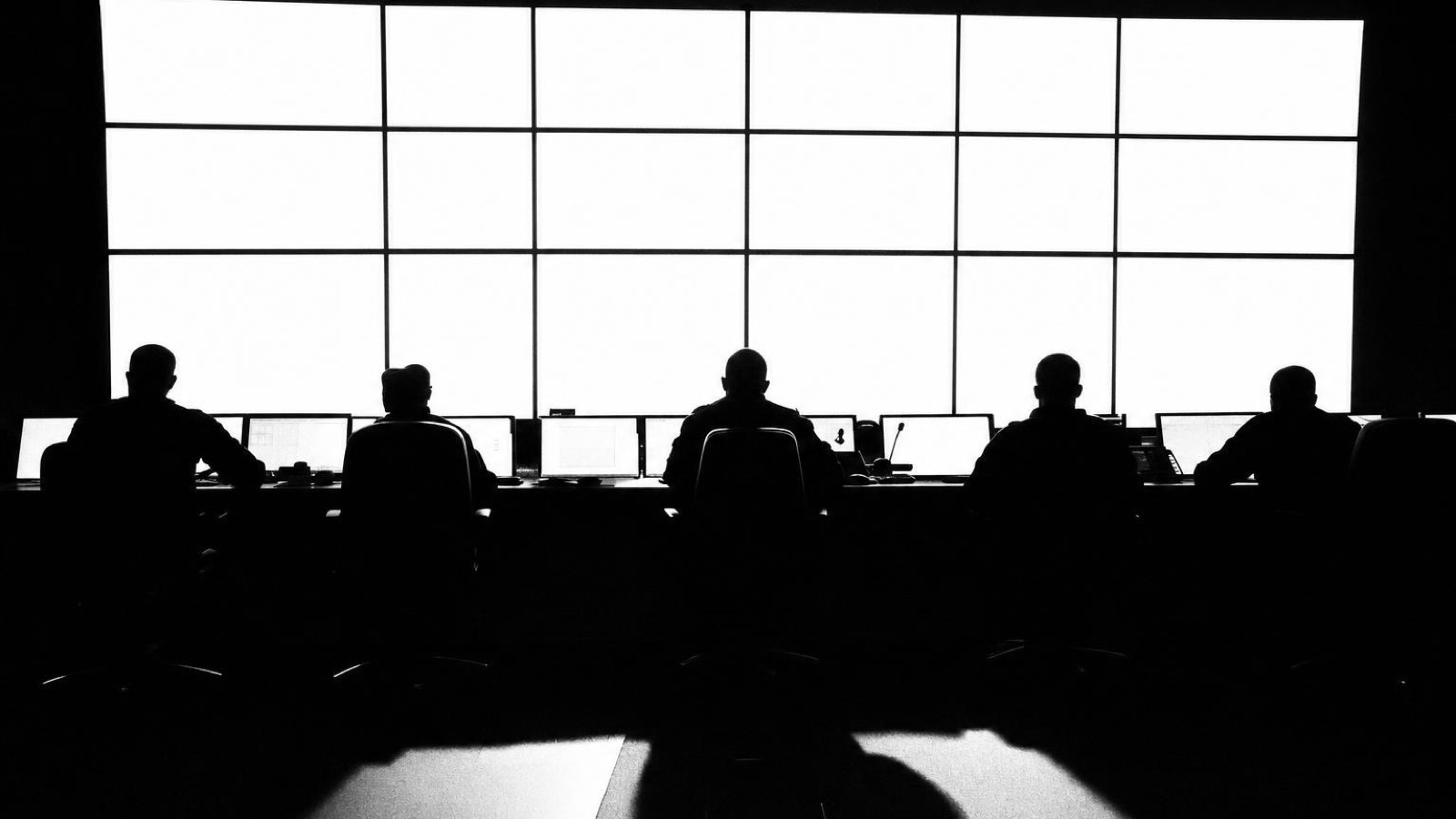 Silhouettes at a control desk against a wall of windows