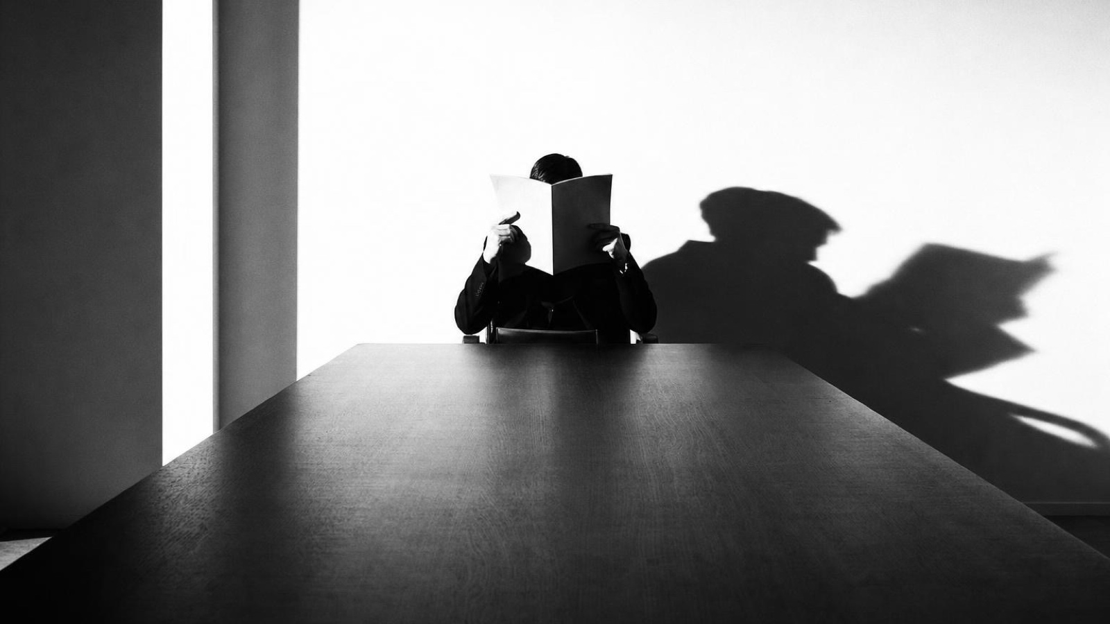 Someone reading at a table, their shadow thrown on the wall behind