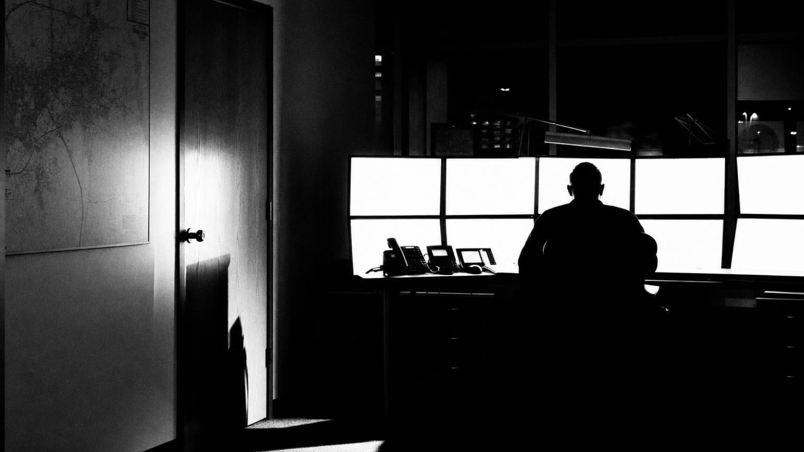 Someone at a desk in a dark office beside a run of windows