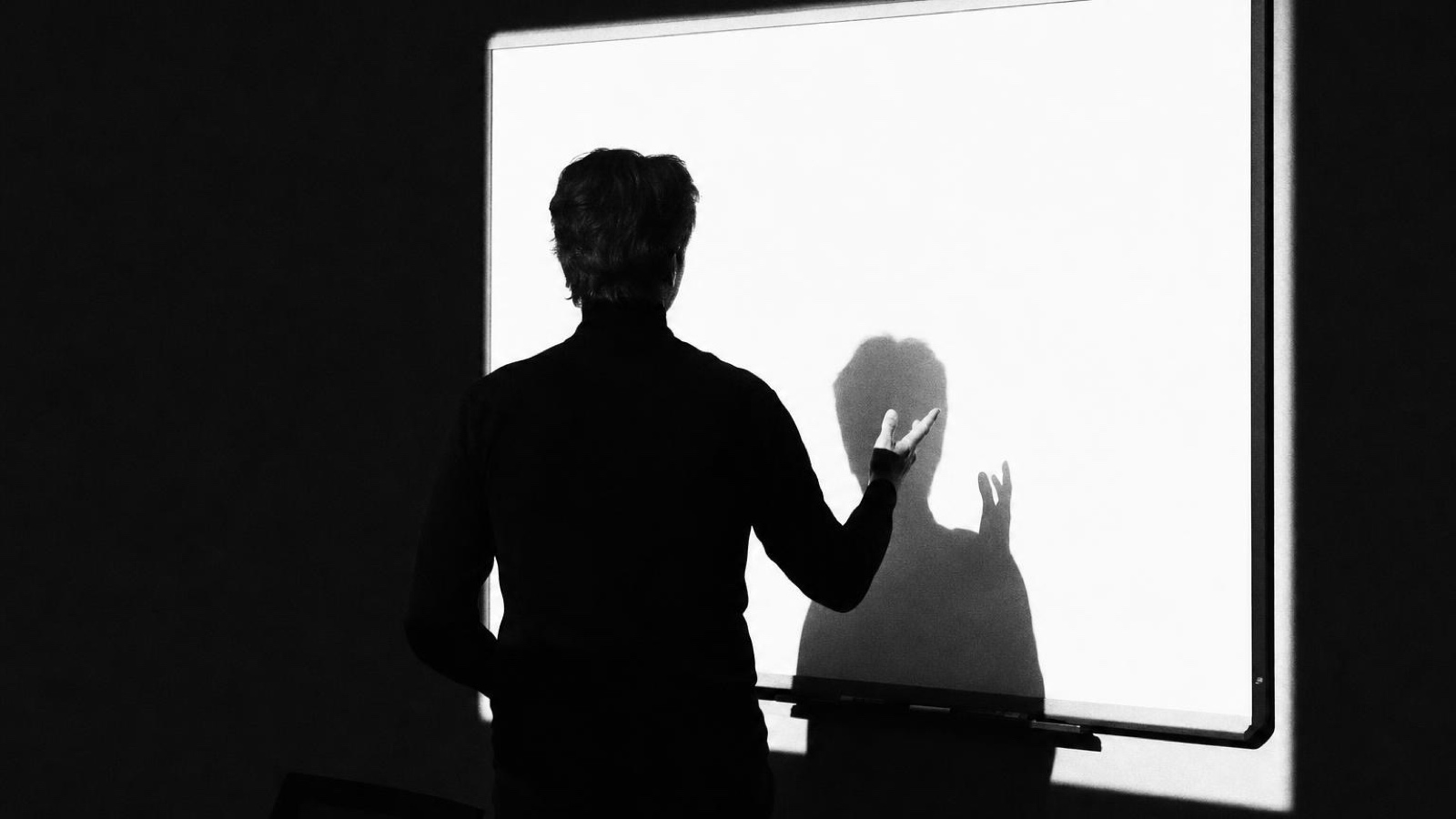 Someone at a lit screen with both hands raised, shadow behind them