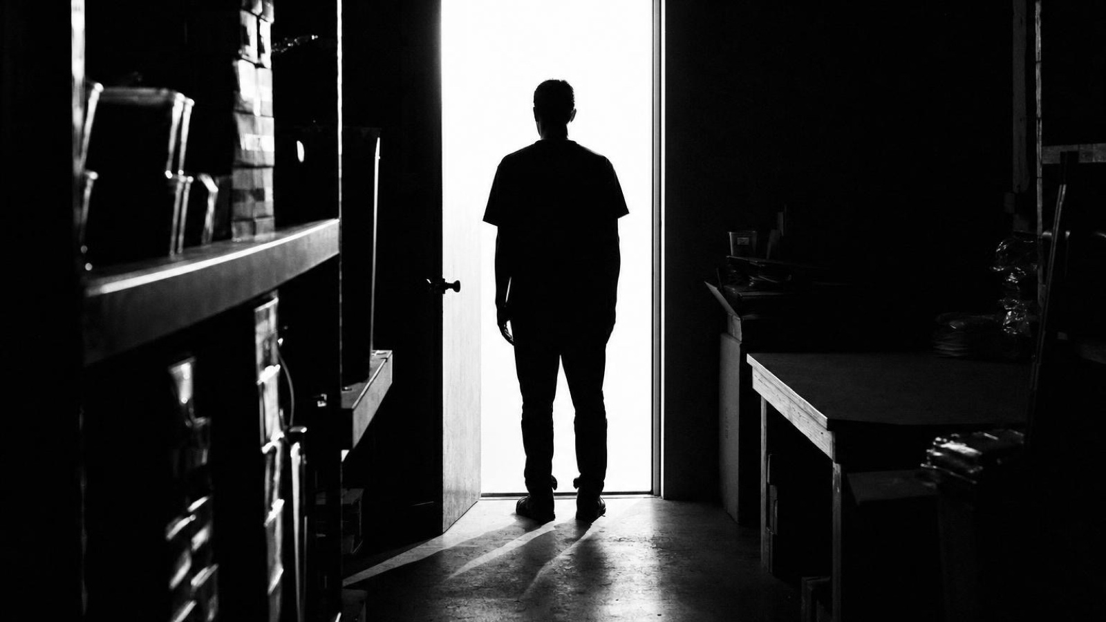 A figure standing in a lit doorway beside shelving